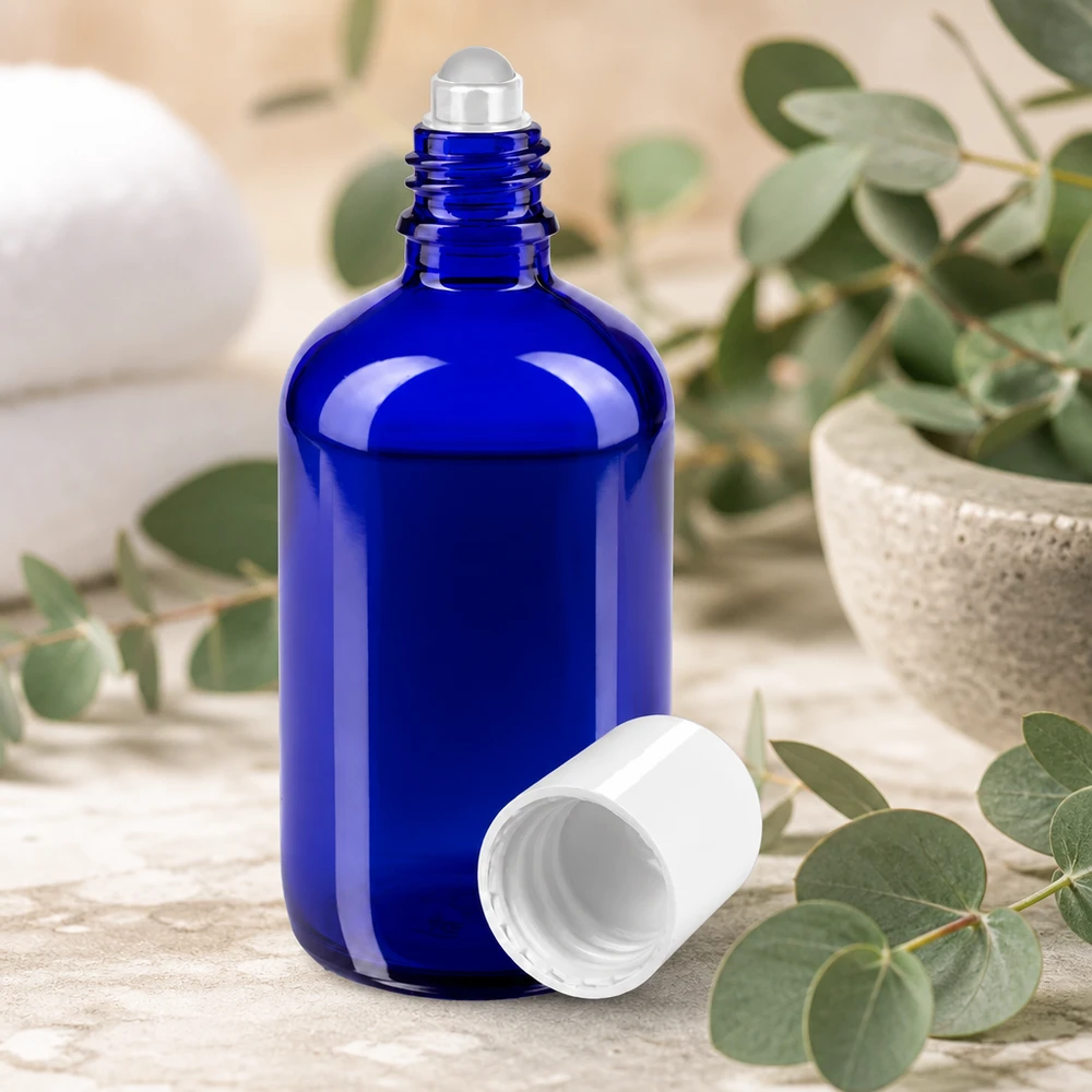 Flacone roll-on da 100 ml di colore blu con sfera in acciaio e tappo bianco, tra rami di eucalipto