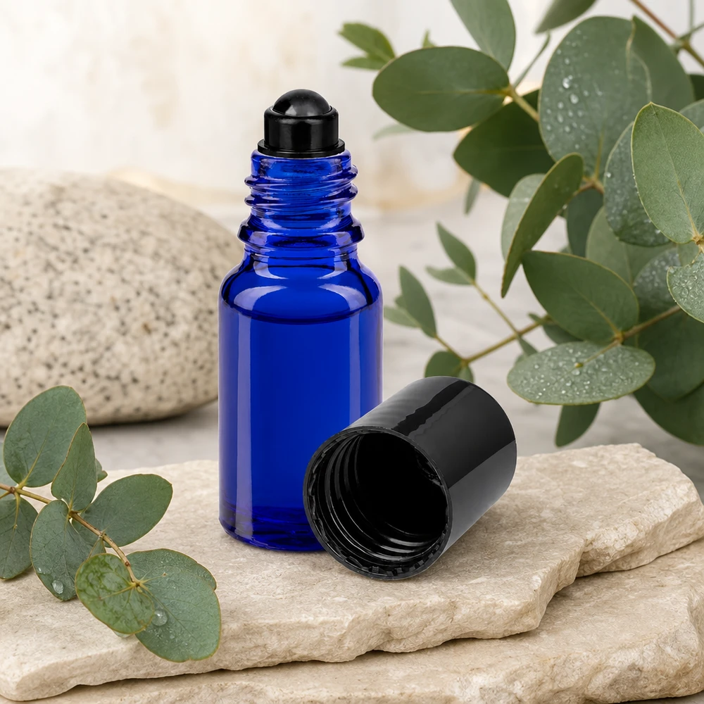 Flacone per deodorante stick in vetro blu 10 ml, roll-on vuoto Flacone roll-on ApoGlas blu da 10 ml con tappo nero, accanto a ramoscelli di eucalipto su una pietra naturale