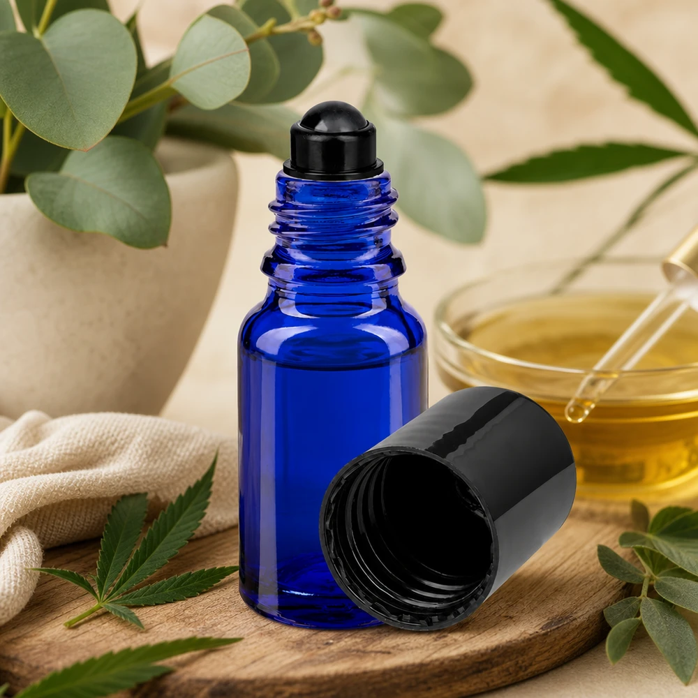 Flacone per deodorante stick in vetro blu 10 ml, roll-on vuoto Flacone roll-on ApoGlas blu da 10 ml con tappo nero su un tagliere di legno, accanto a una foglia di cannabis e a un ramoscello di eucalipto
