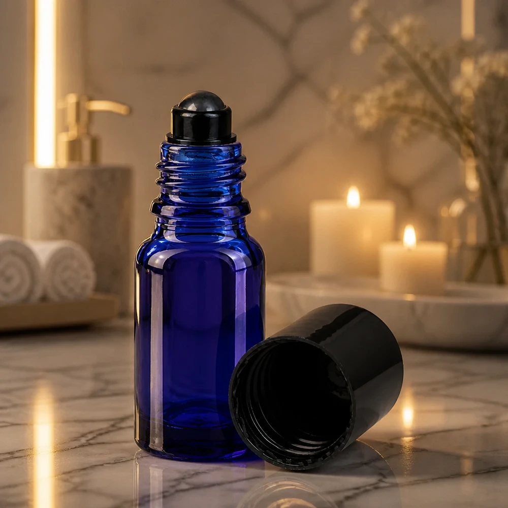 Flacone roll-on da 10 ml blu cobalto con sfera rotante nera, illuminato dalla suggestiva luce delle candele su una superficie di marmo