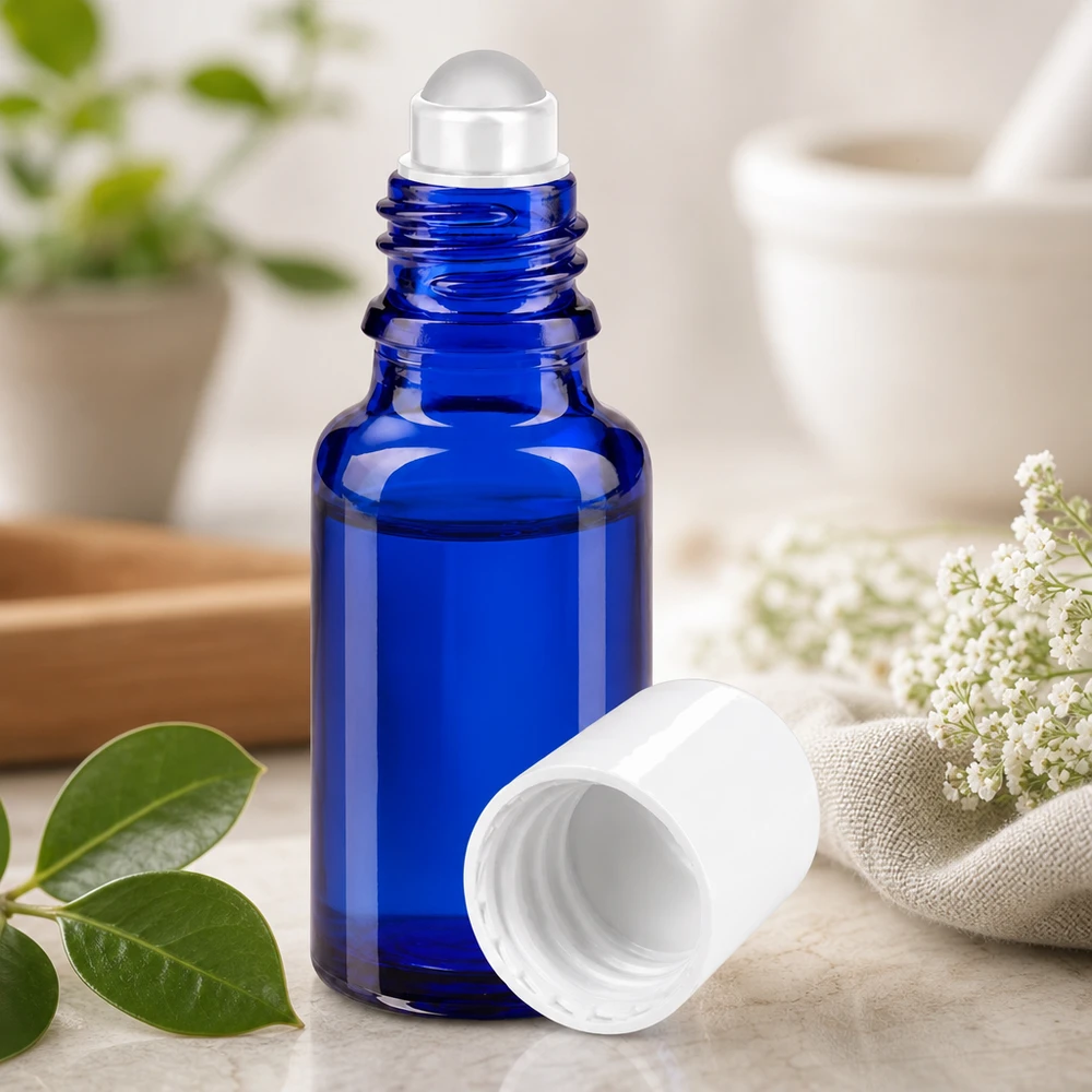 Fiala di vetro da farmacia blu da 20 ml con sferetta trasparente, accanto a fiori bianchi e foglie verdi
