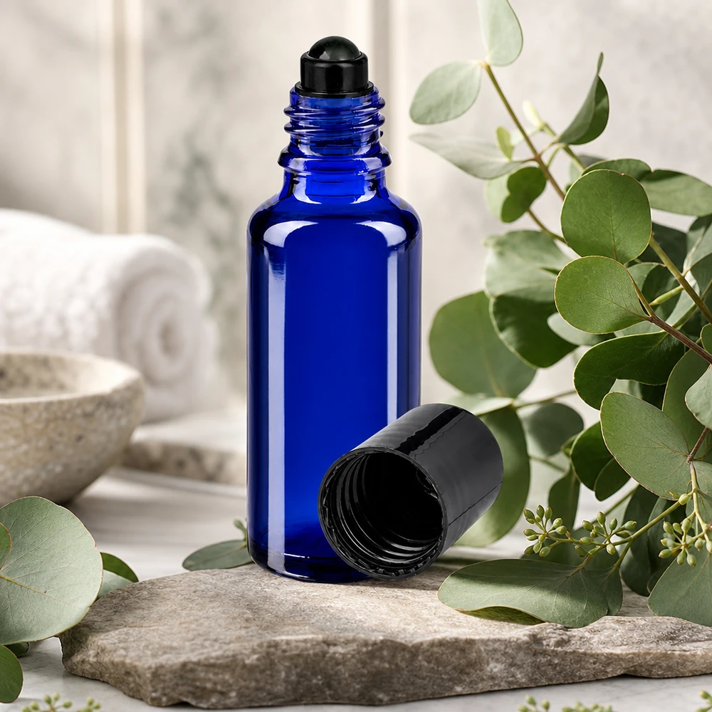 Flacone di vetro da 30 ml blu cobalto con applicatore roll-on nero su una pietra naturale tra rami di eucalipto