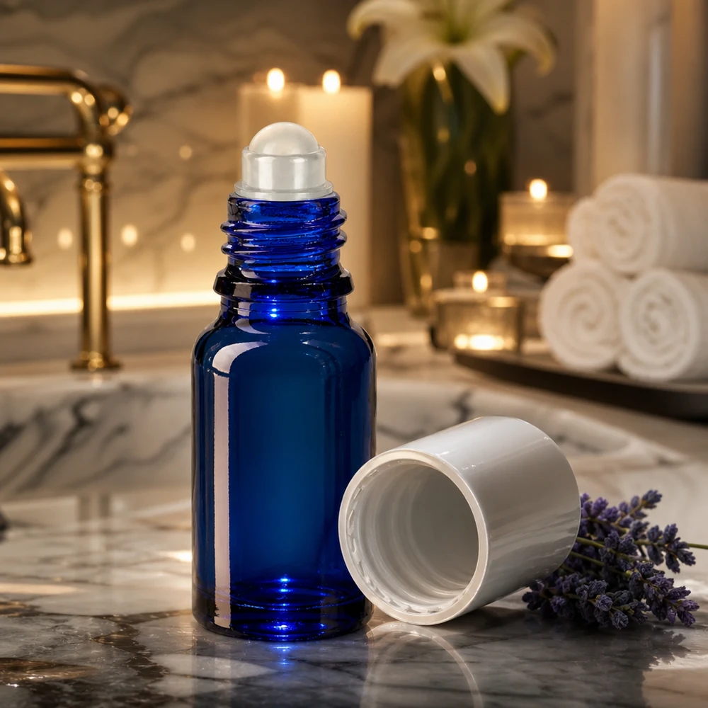 Flacone roll-on da 10 ml blu cobalto con applicatore a sfera su fondo marmorizzato, accanto a fiori di lavanda