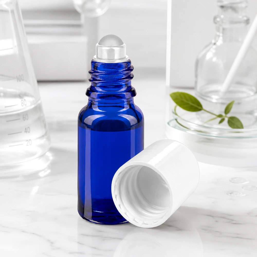 Flacone roll-on da 10 ml blu cobalto con sfera di vetro trasparente e tappo bianco su sfondo marmorizzato