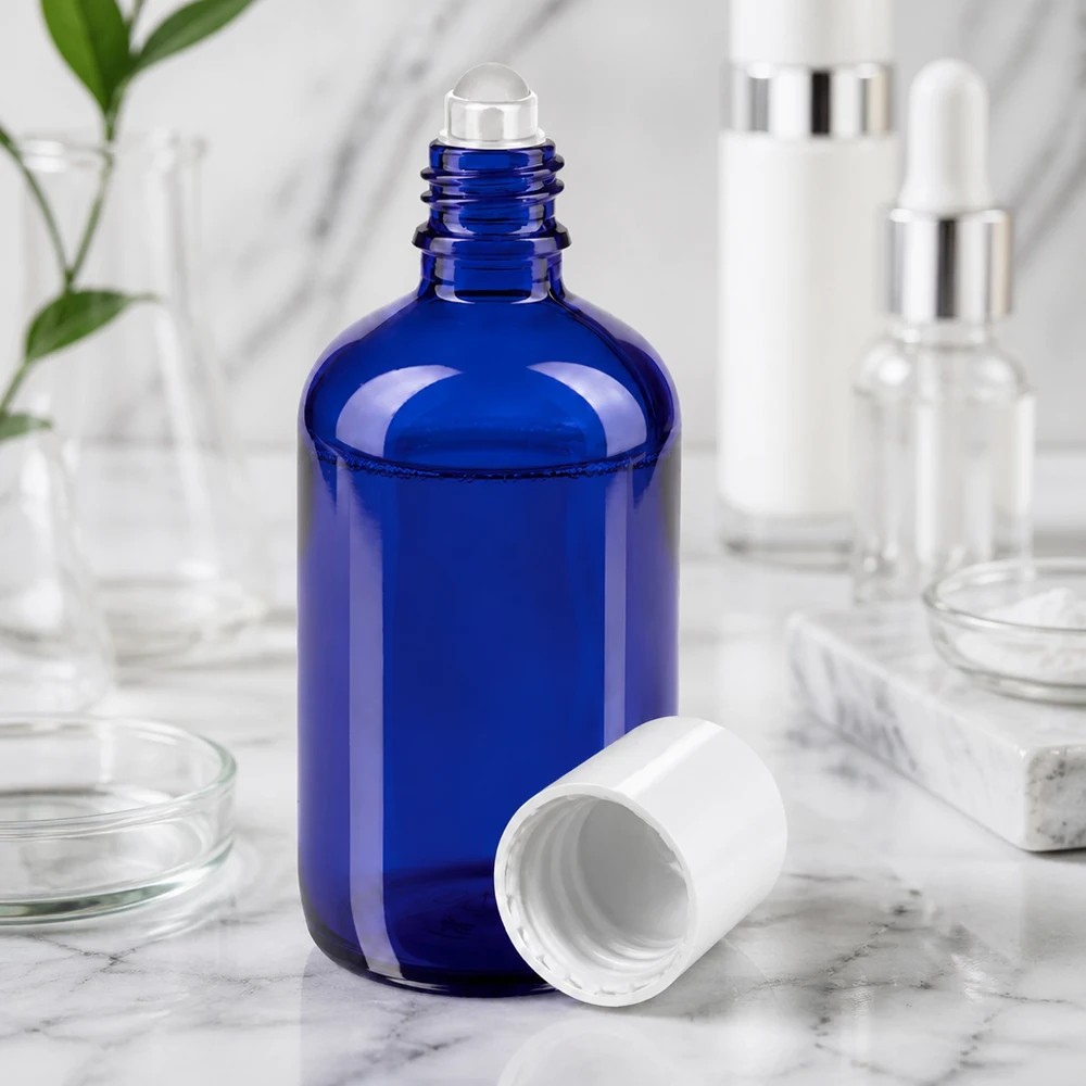 Flacone di vetro blu da 100 ml con sfera rotante e tappo bianco su superficie marmorizzata
