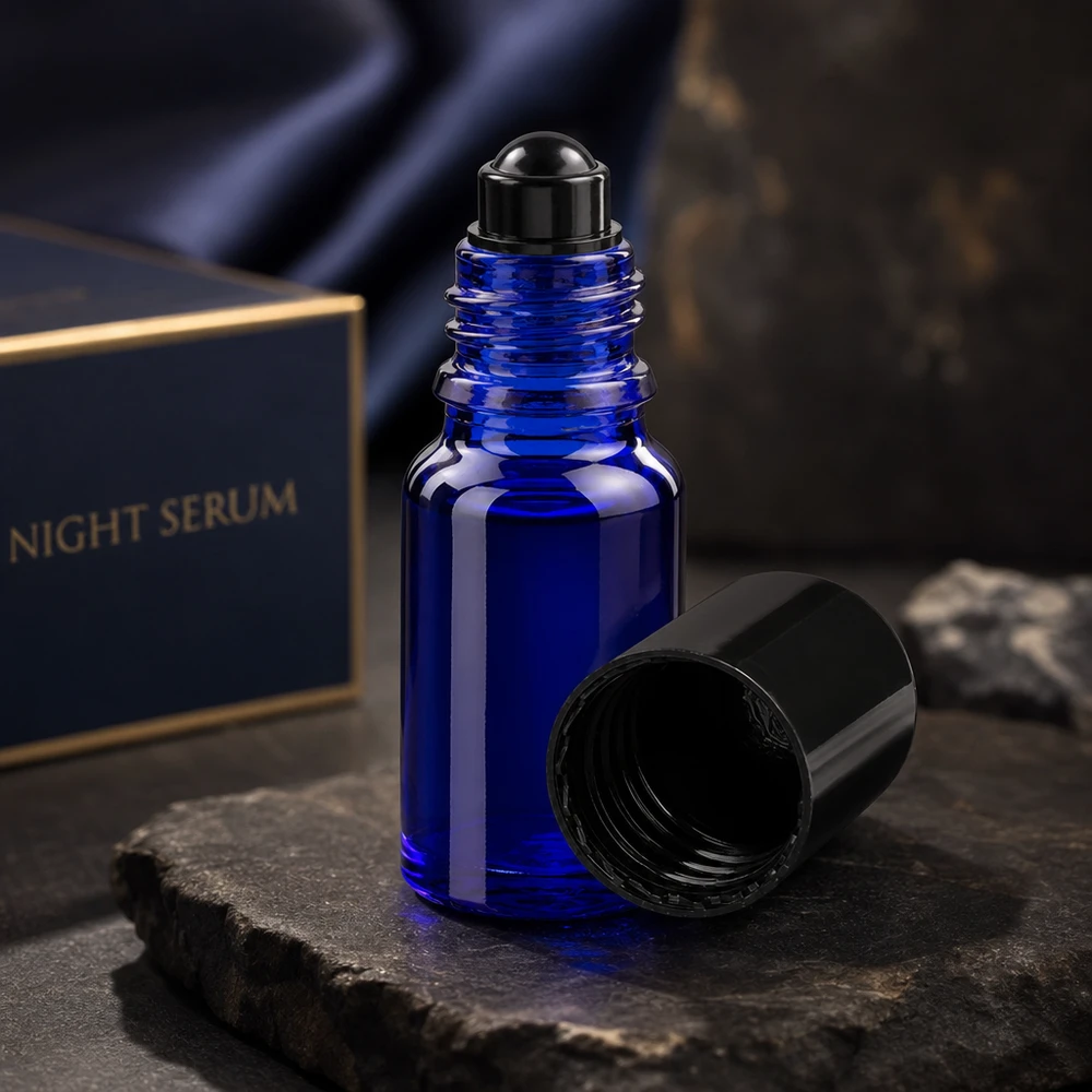 Flacone per deodorante stick in vetro blu 10 ml, roll-on vuoto Flacone roll-on ApoGlas da 10 ml blu scuro con tappo nero aperto su una pietra di ardesia davanti alla confezione del siero da notte